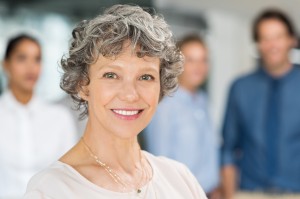 Senior businesswoman smiling and standing in front of a group of businesspeople. Portrait of a smiling business woman looking at camera. Close up of mature businesswoman with happy colleagues.